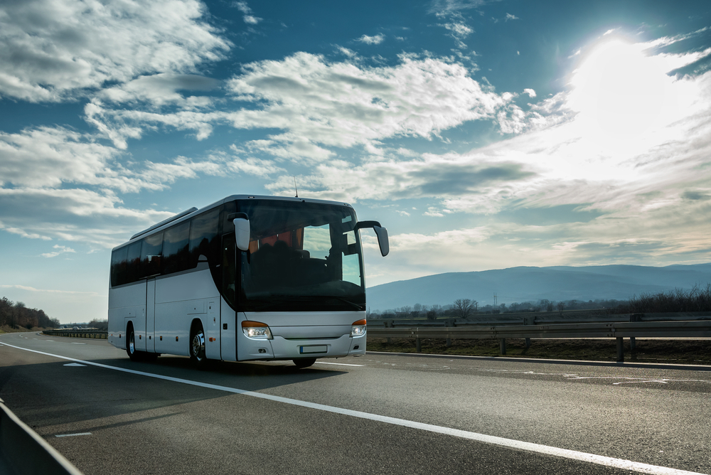 Bus wisata putih modern yang nyaman mengemudi melalui jalan raya saat matahari terbenam yang cerah.